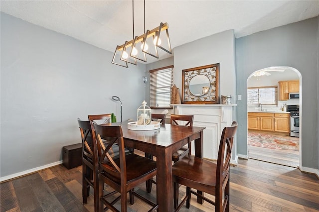 dining space featuring arched walkways, dark wood finished floors, baseboards, and a wealth of natural light