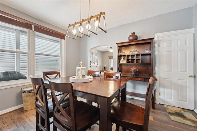 dining space featuring dark wood-style flooring, arched walkways, ceiling fan, and baseboards