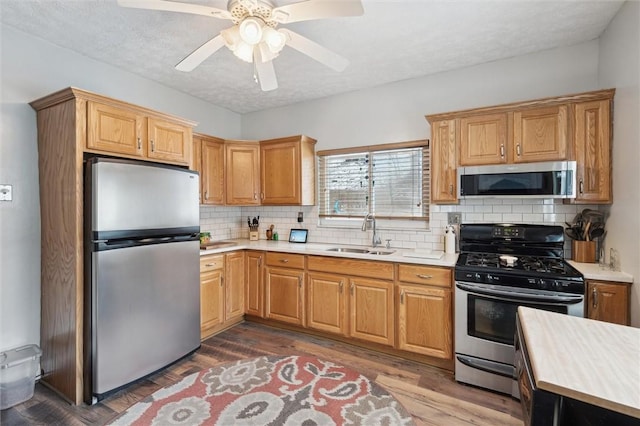 kitchen featuring dark wood finished floors, decorative backsplash, stainless steel appliances, a sink, and light countertops