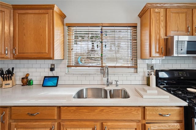 kitchen with brown cabinetry, decorative backsplash, black stove, stainless steel microwave, and a sink