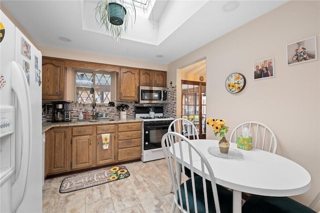 kitchen featuring a skylight, range with gas cooktop, stainless steel microwave, light countertops, and white refrigerator with ice dispenser