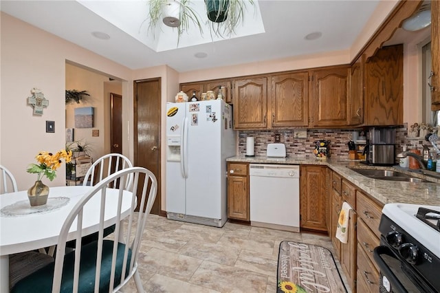 kitchen with white appliances, brown cabinetry, light stone countertops, and a sink