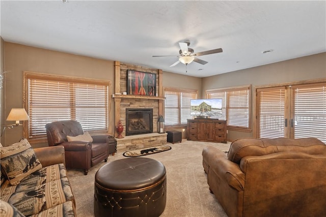 carpeted living room with ceiling fan and a stone fireplace