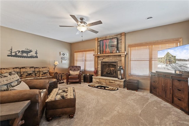 carpeted living room featuring a stone fireplace and ceiling fan