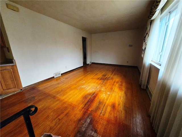 unfurnished room featuring wood finished floors, visible vents, and baseboards