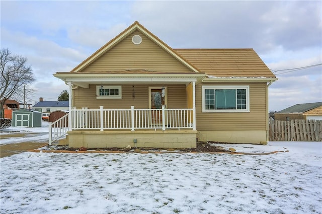 snow covered rear of property with a storage shed and a porch