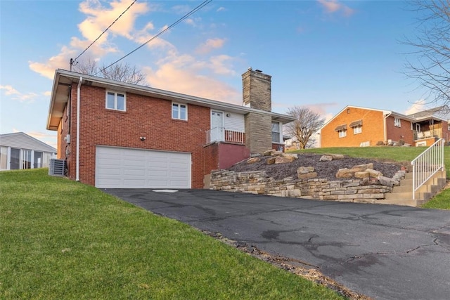 exterior space with aphalt driveway, a garage, brick siding, a lawn, and a chimney