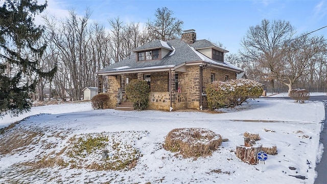 snow covered property with a storage shed, an outbuilding, and stone siding