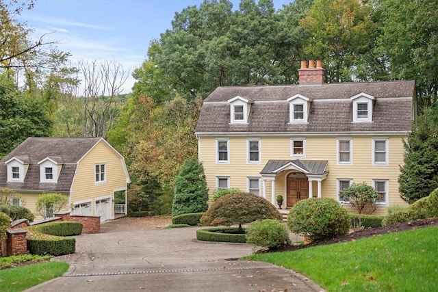 view of front of property with a shingled roof, a chimney, a gambrel roof, concrete driveway, and an attached garage