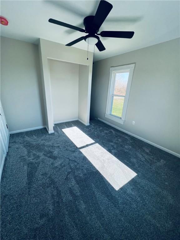 unfurnished bedroom with baseboards, dark colored carpet, a ceiling fan, and a closet