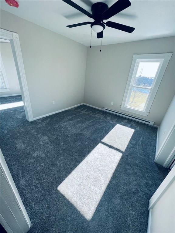 spare room with a baseboard radiator, baseboards, a ceiling fan, and dark carpet