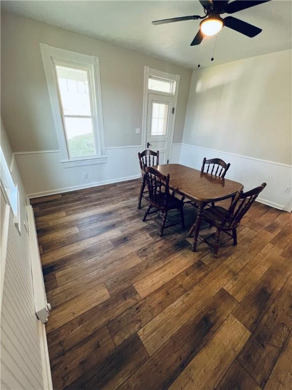 dining space featuring ceiling fan, dark wood-style floors, and a wainscoted wall