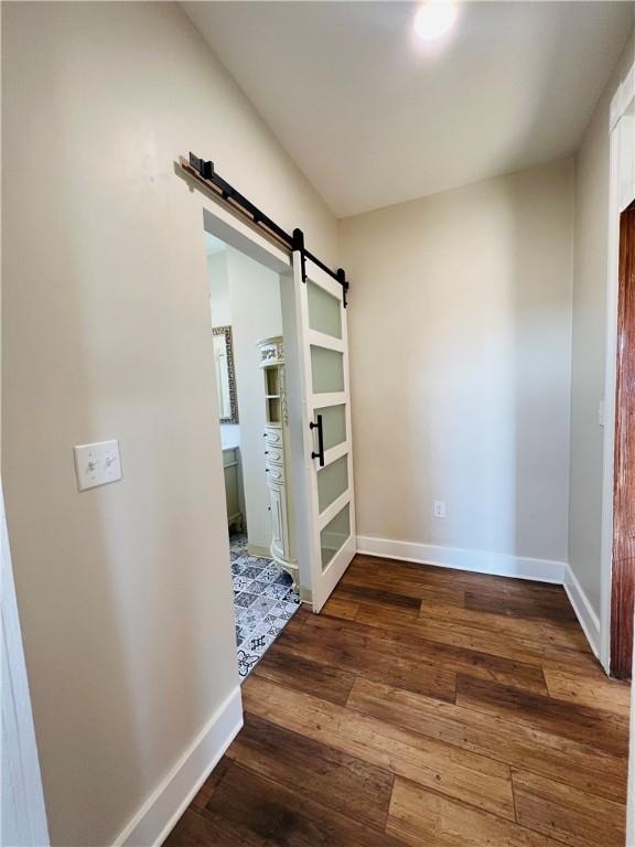 hall featuring baseboards, dark wood-style flooring, and a barn door