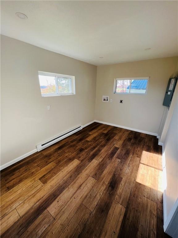 unfurnished room with a wealth of natural light, baseboards, baseboard heating, and dark wood finished floors