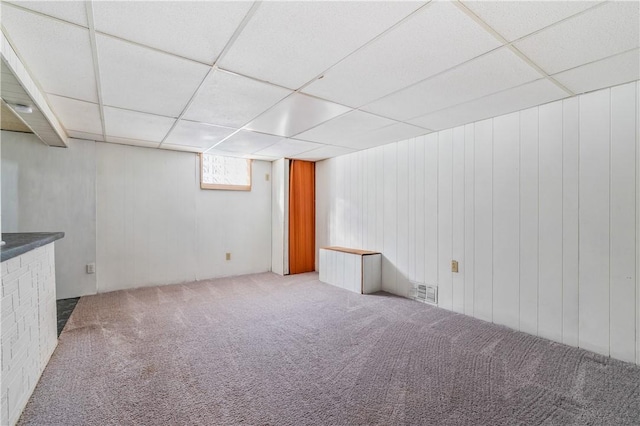 basement with carpet, visible vents, wood walls, and a paneled ceiling