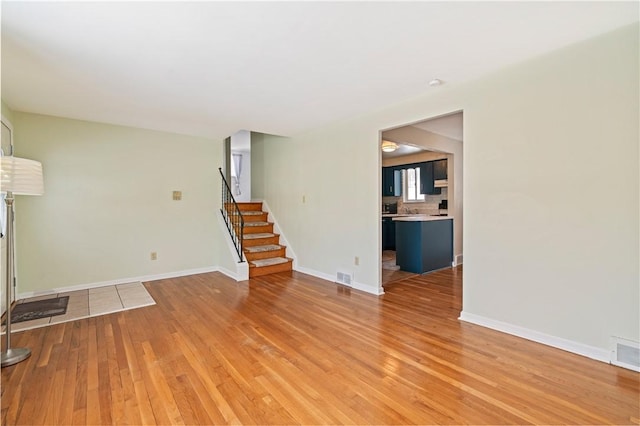 unfurnished living room featuring stairs, baseboards, wood finished floors, and visible vents