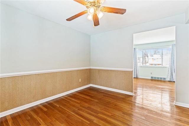 empty room featuring wainscoting, baseboards, visible vents, a ceiling fan, and wood finished floors