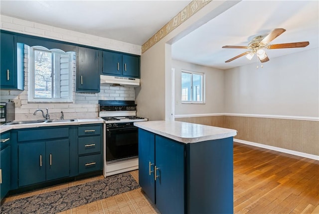 kitchen featuring a sink, backsplash, stove, light countertops, and under cabinet range hood