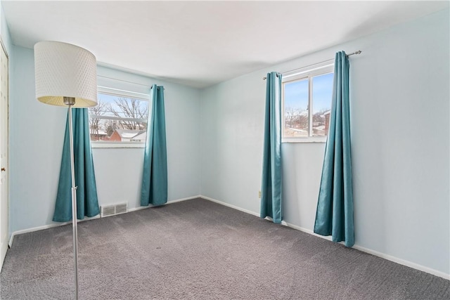 carpeted empty room featuring baseboards, visible vents, and a healthy amount of sunlight