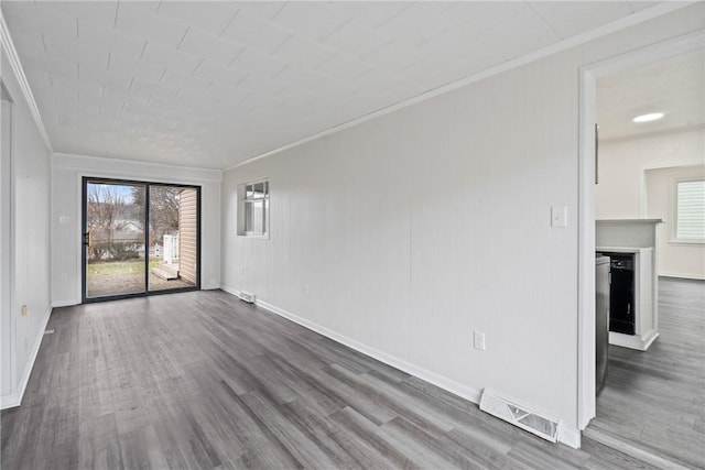 empty room with a fireplace, wood finished floors, visible vents, baseboards, and crown molding