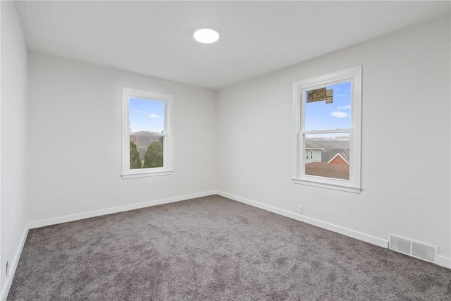 unfurnished room featuring dark colored carpet, a wealth of natural light, visible vents, and baseboards