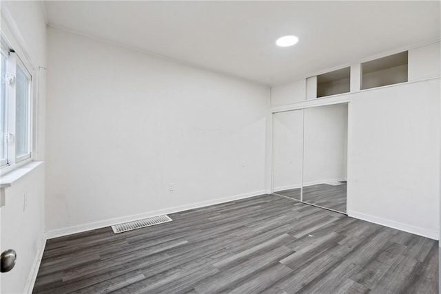 unfurnished bedroom featuring dark wood-style flooring, a closet, visible vents, and baseboards