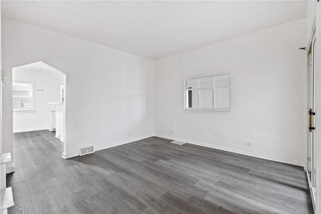 spare room featuring baseboards, visible vents, arched walkways, and dark wood-style flooring