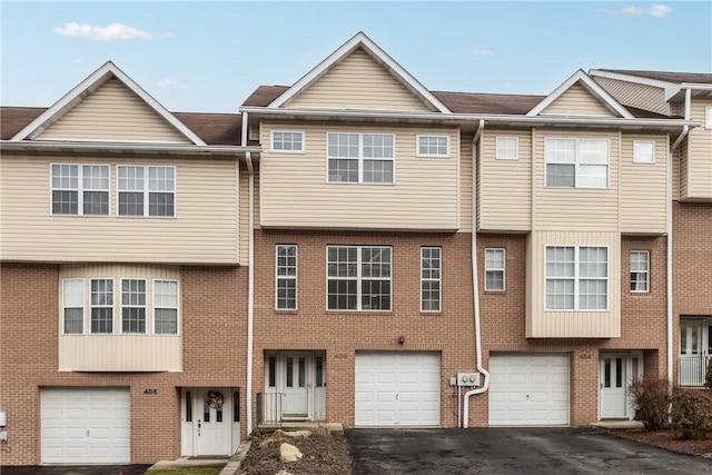 view of property featuring driveway, an attached garage, and brick siding