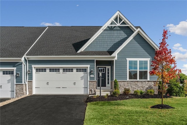 craftsman inspired home featuring an attached garage, stone siding, driveway, roof with shingles, and a front yard