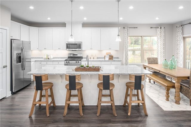 kitchen with stainless steel appliances, white cabinets, hanging light fixtures, and light stone counters