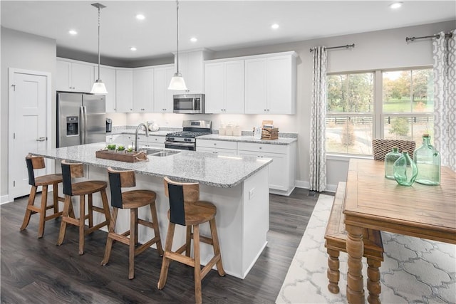 kitchen featuring a kitchen island with sink, stainless steel appliances, a sink, white cabinetry, and pendant lighting