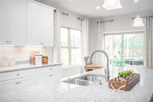 kitchen with light stone counters, white cabinetry, pendant lighting, a sink, and recessed lighting