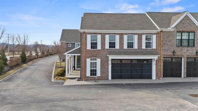 view of front of home with driveway, brick siding, and roof with shingles