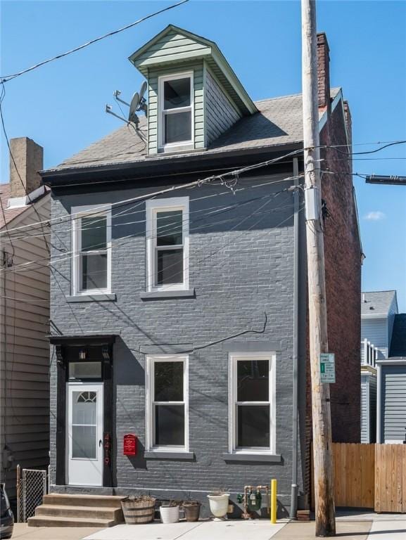 view of front facade featuring a chimney, fence, and brick siding