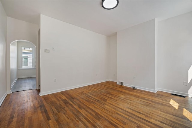 spare room with arched walkways, dark wood-style flooring, visible vents, and baseboards