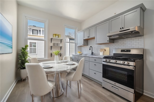 kitchen with light countertops, decorative backsplash, gray cabinetry, stainless steel gas range, and under cabinet range hood