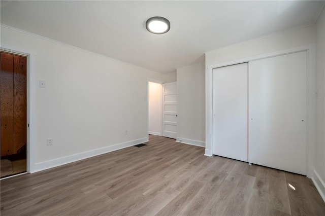 unfurnished bedroom featuring a closet, visible vents, ornamental molding, light wood-type flooring, and baseboards