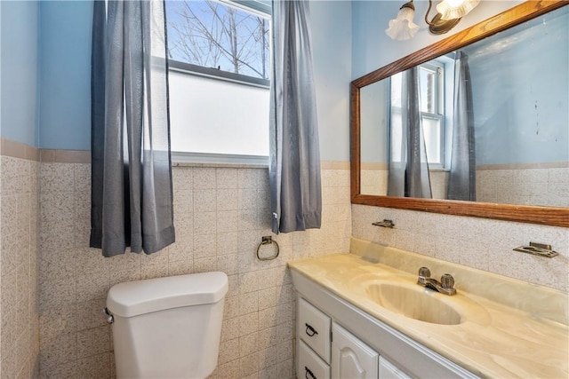 bathroom with toilet, wainscoting, tile walls, and vanity