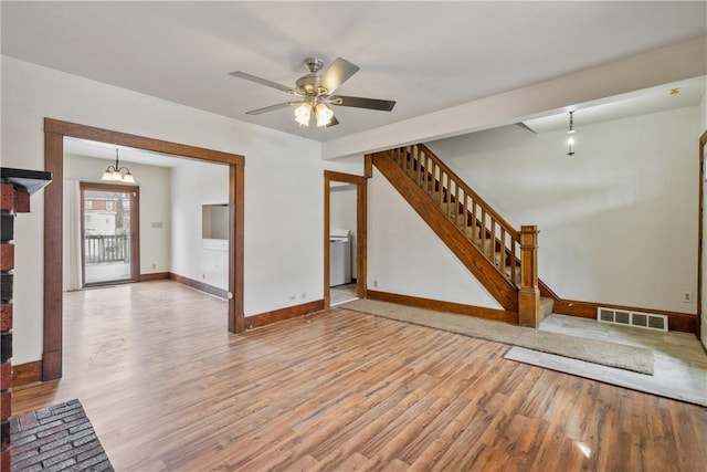 unfurnished living room with light wood-style flooring, ceiling fan with notable chandelier, visible vents, baseboards, and stairs