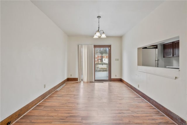 spare room featuring a chandelier, baseboards, and light wood finished floors