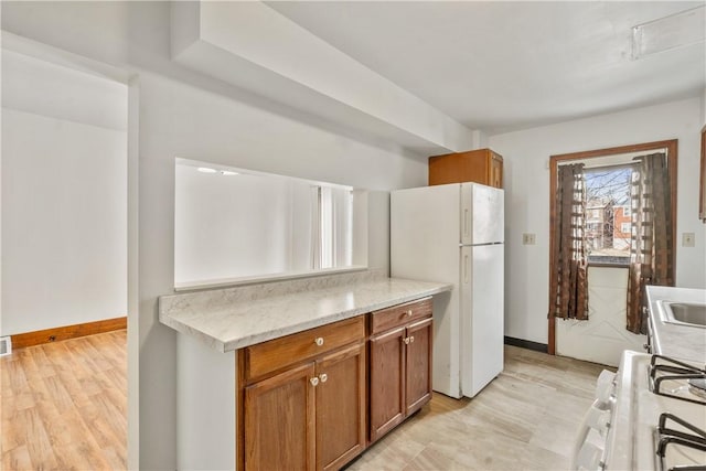 kitchen featuring brown cabinetry, white appliances, and baseboards