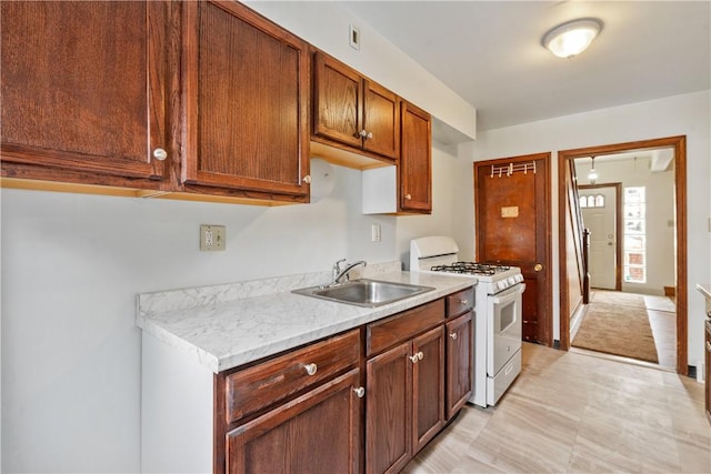 kitchen with white range with gas stovetop, brown cabinets, and a sink