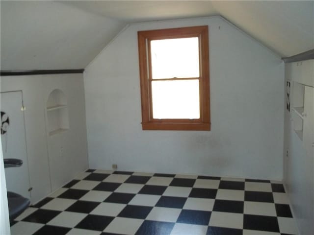 additional living space with vaulted ceiling, dark floors, and built in features