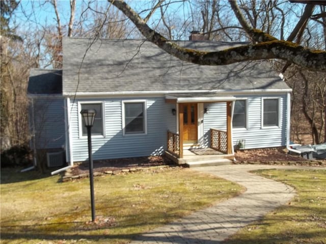 view of front of property featuring roof with shingles, a chimney, central AC unit, and a front yard