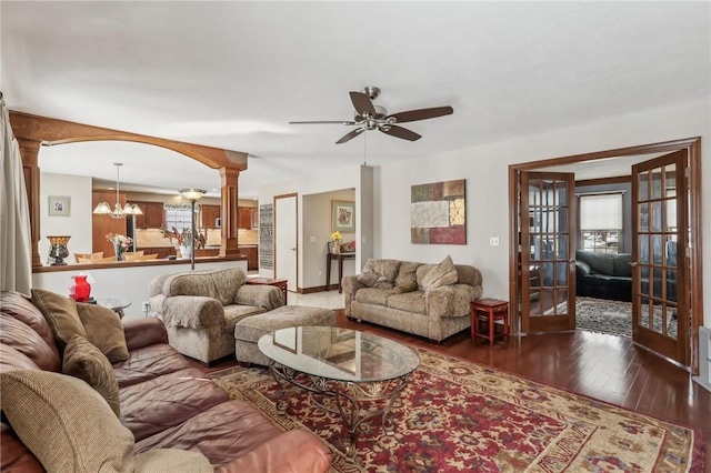 living area featuring ornate columns, arched walkways, dark wood finished floors, and ceiling fan with notable chandelier