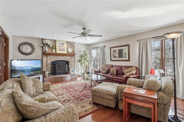 living area with a brick fireplace, ceiling fan, and wood finished floors