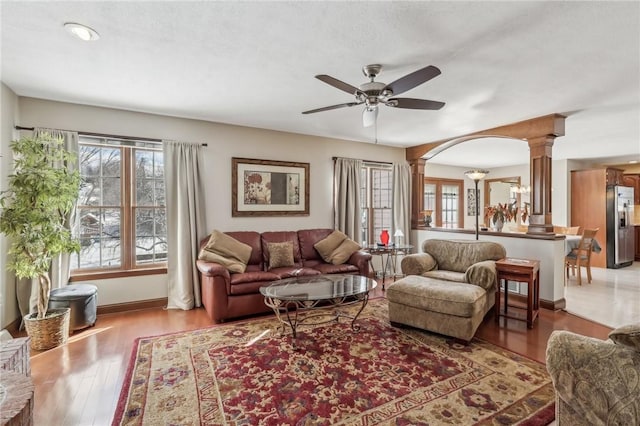 living area featuring light wood-style floors, decorative columns, baseboards, and ceiling fan