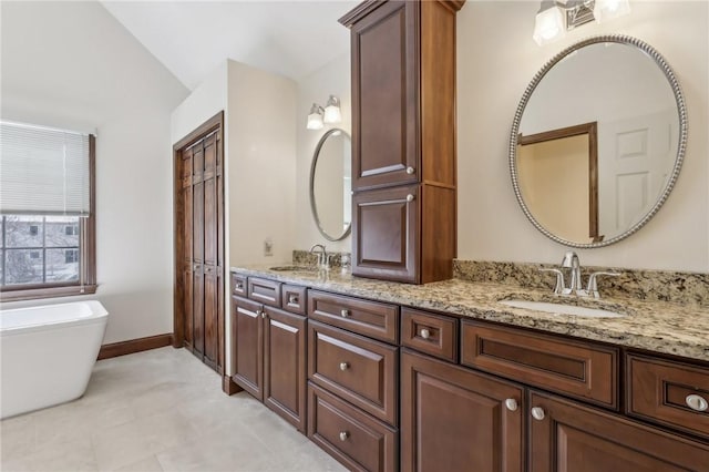 bathroom featuring double vanity, a freestanding bath, baseboards, and a sink