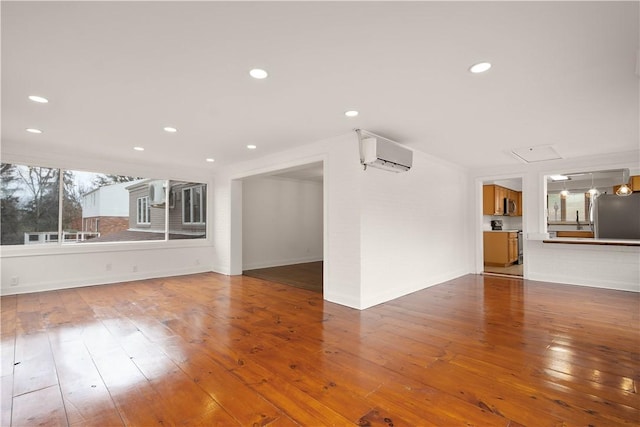 unfurnished living room with baseboards, an AC wall unit, wood finished floors, and recessed lighting