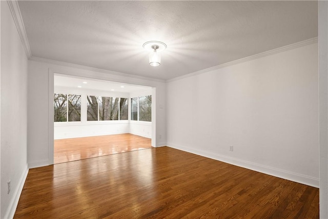 spare room featuring baseboards, wood finished floors, and crown molding